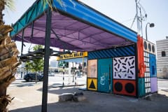 An abandoned gas station building has been redone in very colorful pop art style, with bold hues, black stripes and shapes, and black and white gridwork.