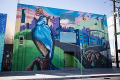 A cartoon blue bird holds a key in its beak and looks out over a cartoon Las Vegas landscape that includes a giant turtle with windows in its shell.