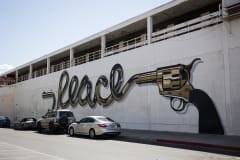 A mural on a white wall depicting a gold bullet discharged from an old, gold six-shooter, spelling out “peace” in a stylish old west style script.