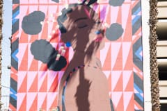 A black woman with Afro puffs tilts her head over her right shoulder as though she's enjoying the sun on her face. Behind her is a grid of pink and red triangles.