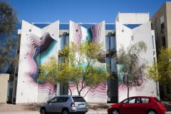 Fading, curved lines from pinks to blues adorn the outside of a building at various angles, making the entire side of the building appear to be concave and dimentional.