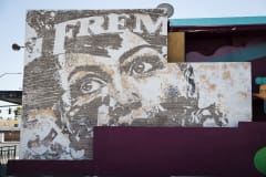 A partial mural on the side of a parking garage in a vintage style, depicting the top half of a face and the letters F-R-E-M.