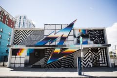 A mural made of a chic combination of black and white geometric shapes with modern rainbow pops of color like a metallic lightening bolt painted on the side of a building.