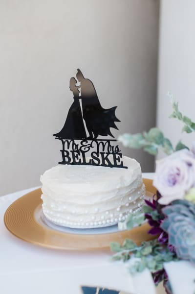 Die cut Batman and bride novelty cake topper with the names "Mr. & Mrs. Belske", placed atop a wedding cake.