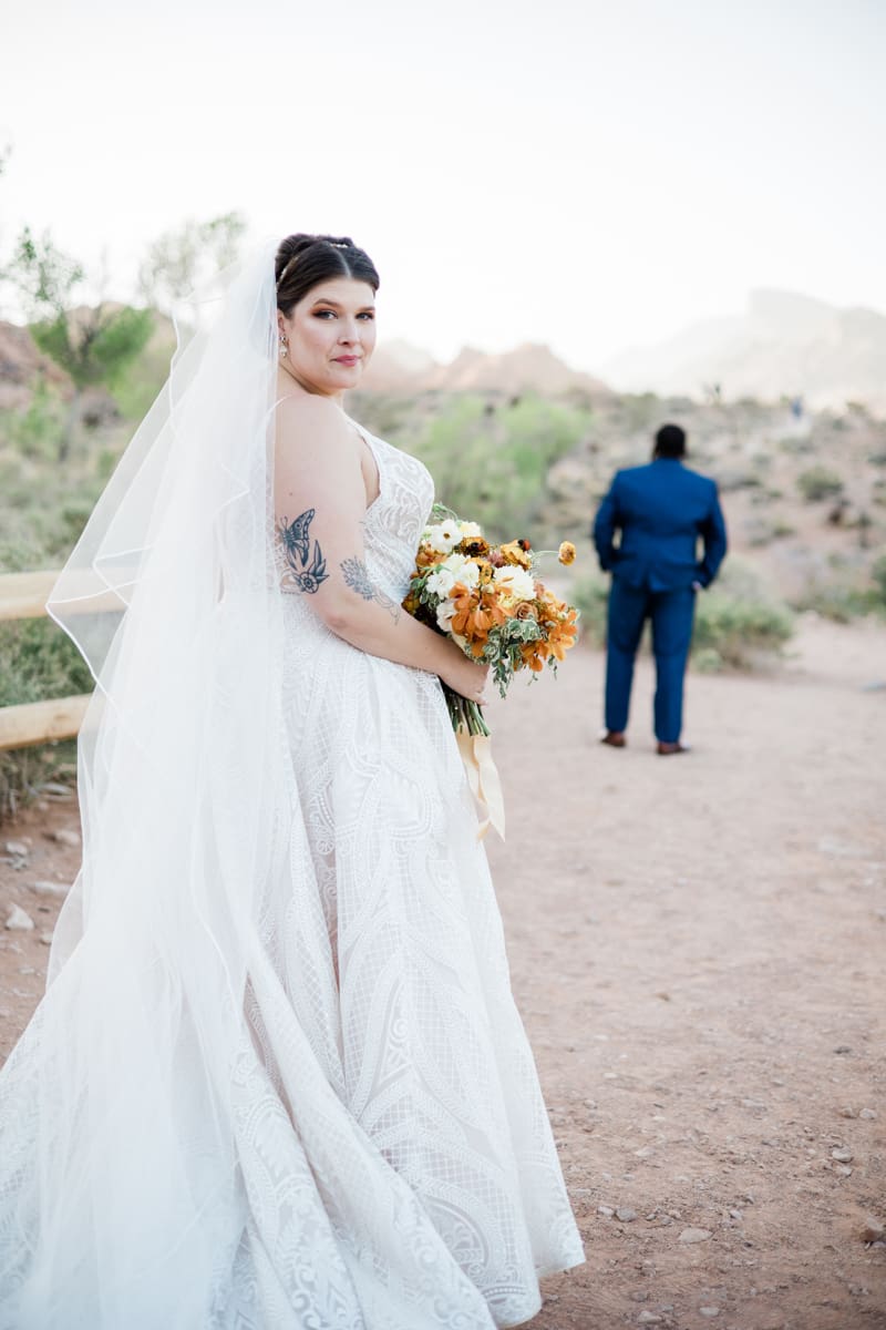 Beautiful bride glancing over her shoulder at the camera while groom stands in the background.