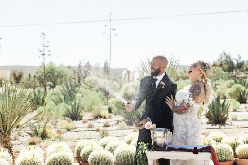 A couple sprays Champagne to celebrate their wedding amongst a collection of barrel cacti and agave.