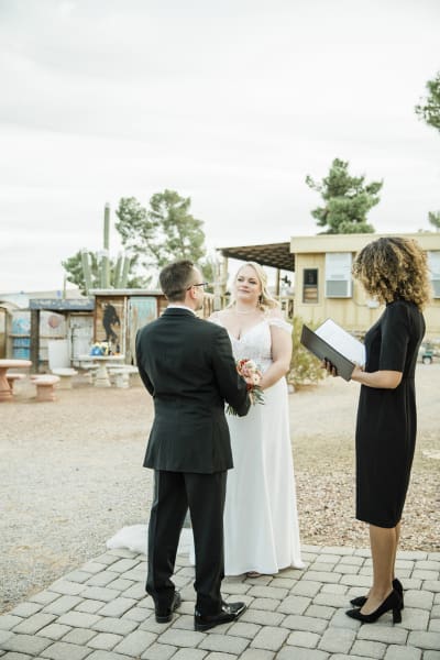 A bride and groom stand before a wedding officiant performing a marriage ceremony on a small brick patio.