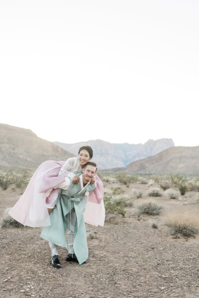 A bride jumps on the back of her groom as they pose for wedding photos in the Mojave Desert.