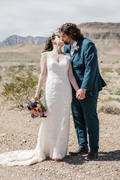 A bride and groom hold hands and kiss on their wedding day in the Mojave Desert.