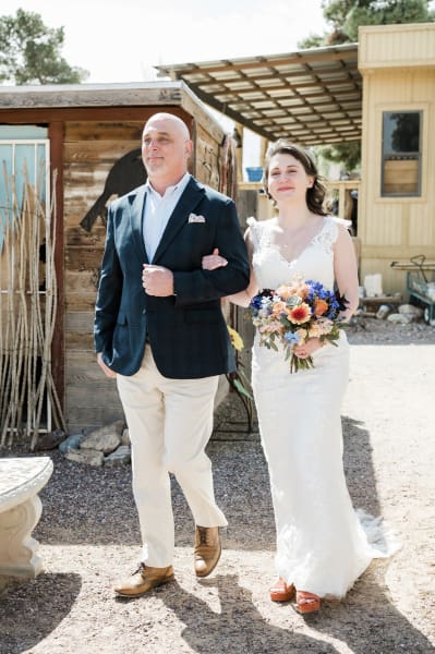 A smiling bride is escorted by a man past some wooden structures at Cactus Joe’s Blue Diamond Nursery.