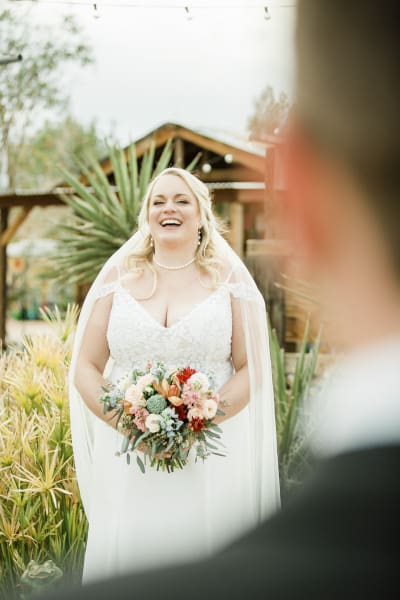 A bride laughs while looking at her groom who is out of focus in the foreground.