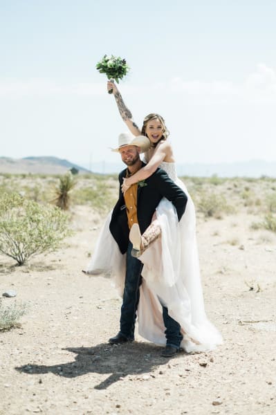 A groom carries his bride piggyback-style as the couple celebrates their wedding in the Mojave Desert.