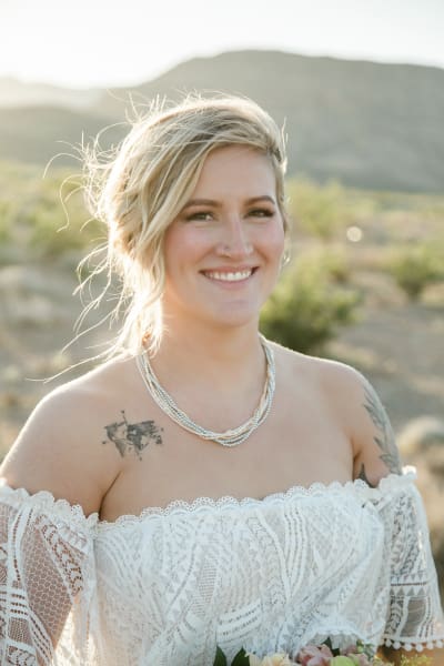 A portrait of a bride wearing a lacy shoulder-less dress standing in the desert.