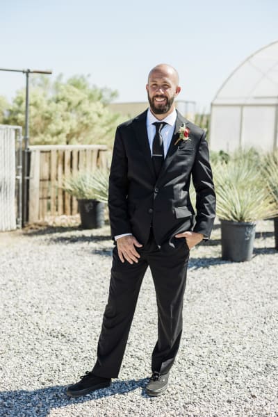 A full body portrait of a groom standing in front of potted cacti.