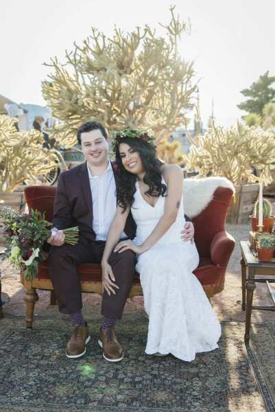 A groom and bride sit on a velvet couch on a sunny day in the garden at Cactus Joe's.