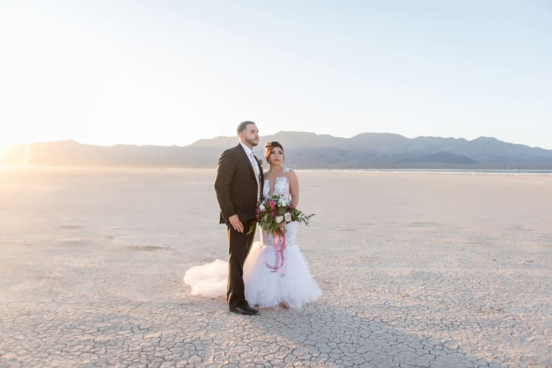 As the sunsets over the mountains behind them , a groom and bride stand boldly as they pose for pictures on their wedding day at the Dry Lake Bed near Las Vegas.