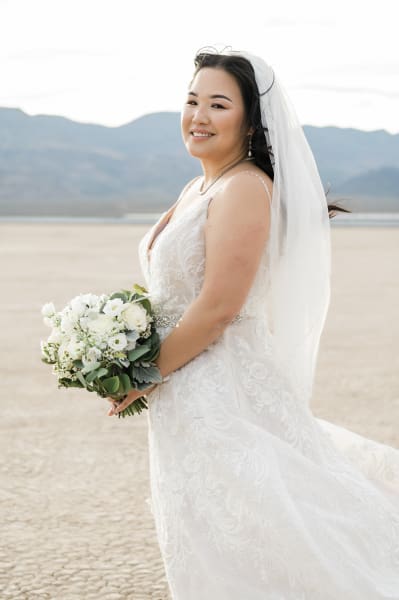A bride poses on her wedding day at the Eldorado Dry Lake Bed. She is standing at a three-quarters angle from the camera. Mountains can be seen in the distance.
