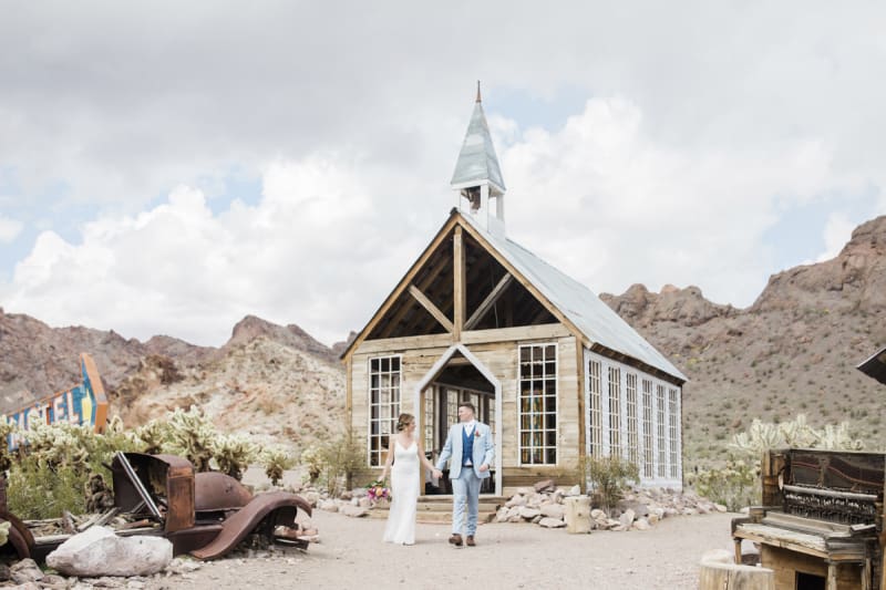 Wide shot of a bride and groom exiting the rustic wooden chapel in Eldorado Canyon.