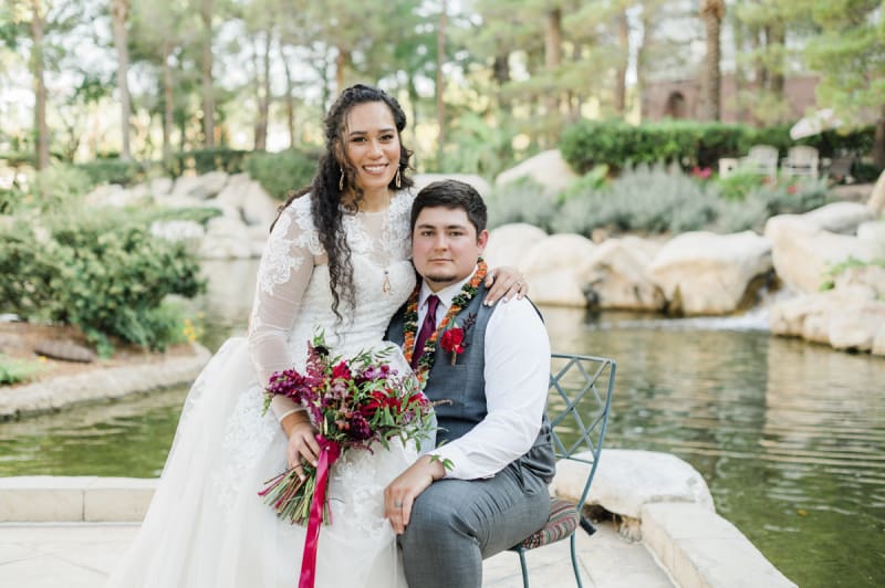 Bride sitting with groom on a rock in front of a pond.