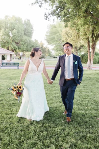 A bride and groom smile at each other and hold hands as they walk through a park in Boulder City, Nevada.