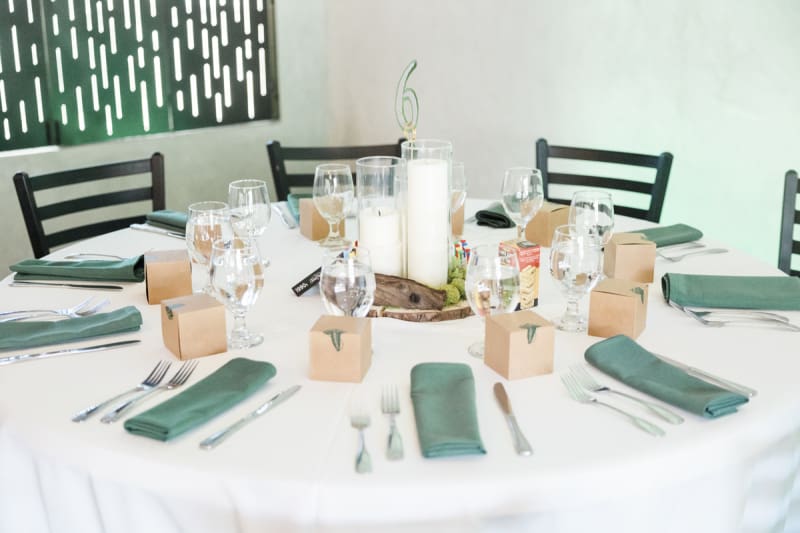 A round table with a white tablecloth is set with place settings which include a small gift box.