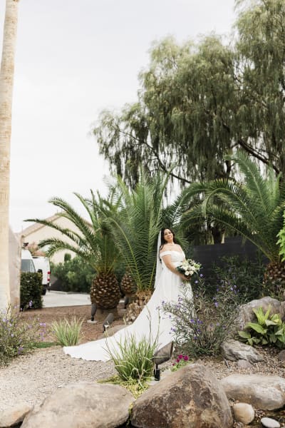 A bride poses for a full-length wedding portrait as she stands in a desert rock garden.