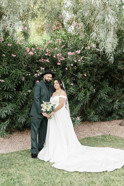 A wide shot of a groom and bride posing in front of a row of pink Oleander bushes.