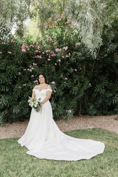A bride's wedding portrait displays the long trail of her wedding dress spread out on the lawn in a garden.