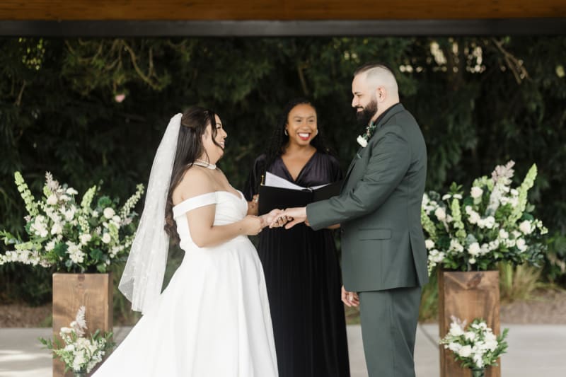 A bride and groom hold hands in front of a wedding officiant who performs their marriage ceremony.
