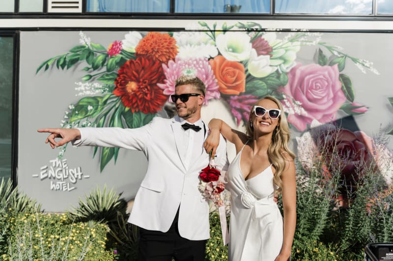 A bride and groom in sunglasses pose for a fun wedding photo in front of a mural of flowers in Downtown Las Vegas.