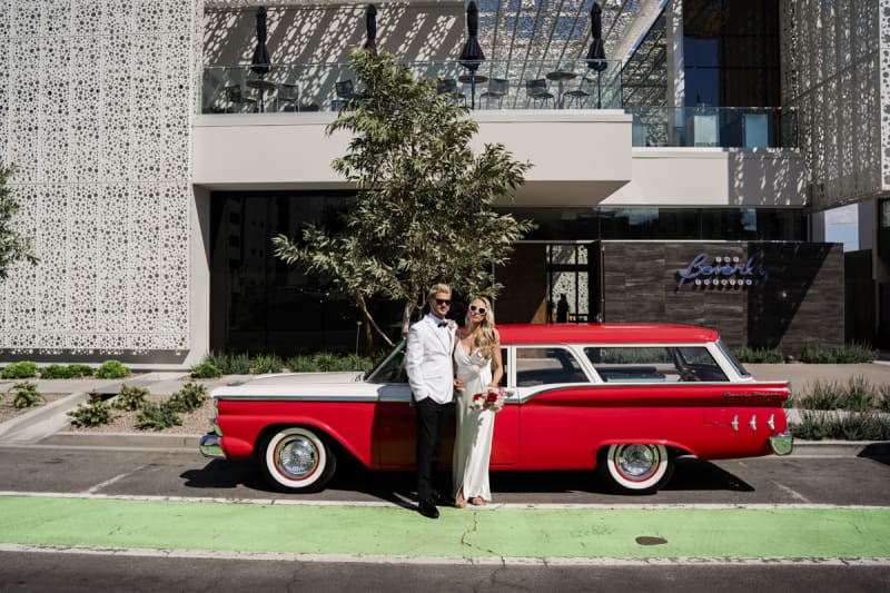 A bride and groom pose with a red and white 1959 Ford Ranch Wagon that's parked in front of the Beverly Theater in Downtown Las Vegas.