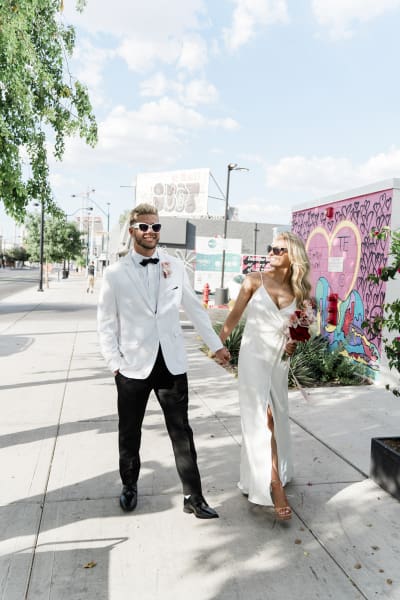 A groom and bride hold hands as they walk towards the camera on a sidewalk in Downtown Las Vegas. 