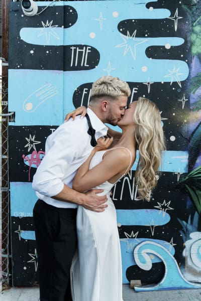 A groom and bride kiss deeply as they pose for wedding photos in front of a wavy and starry black and blue mural in Downtown Las Vegas.