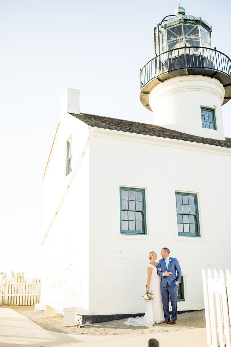 Bride and groom stand looking at each other in front of Point Loma lighthouse.