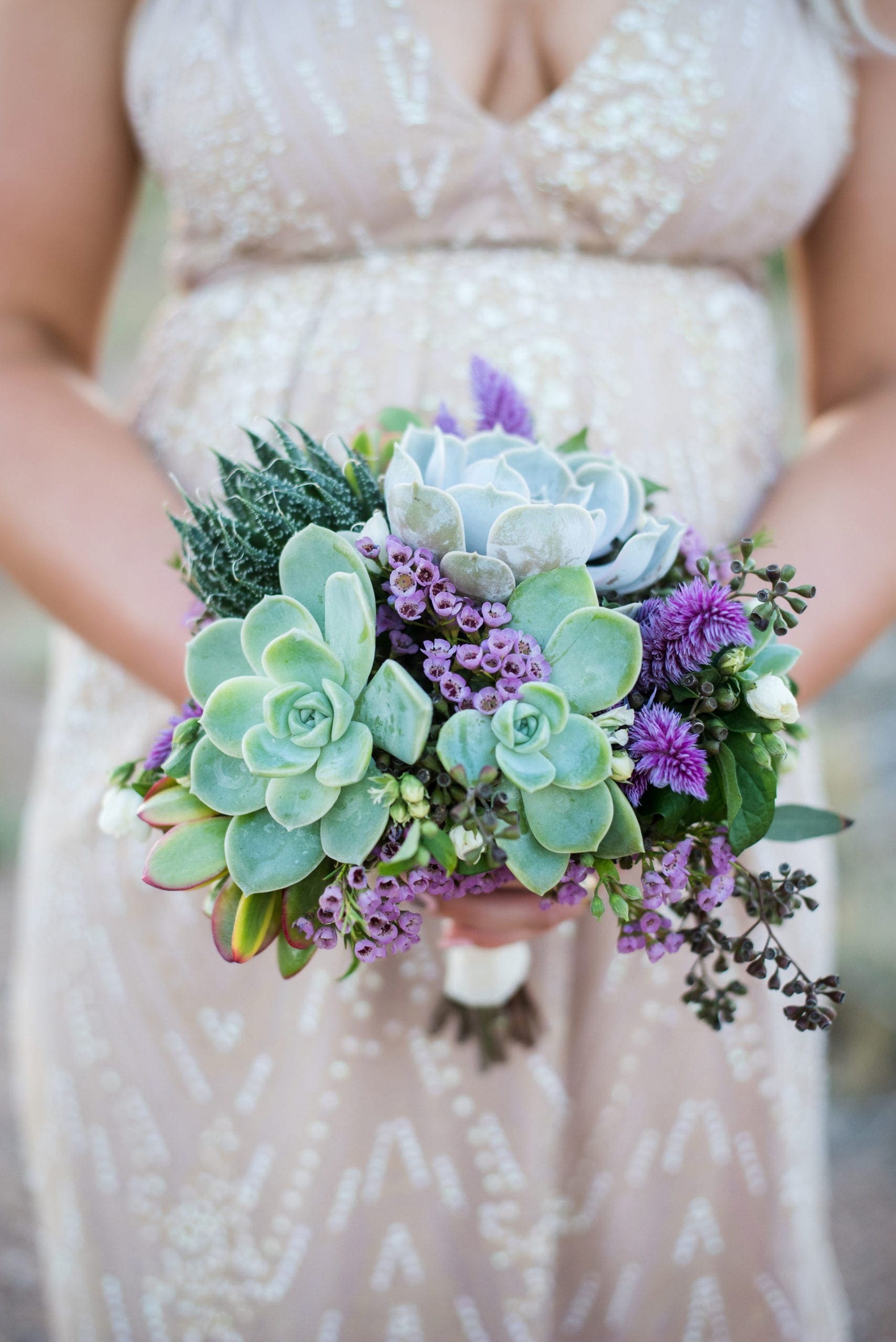Bride in a white lace dress holding a green and purple wedding bouquet.