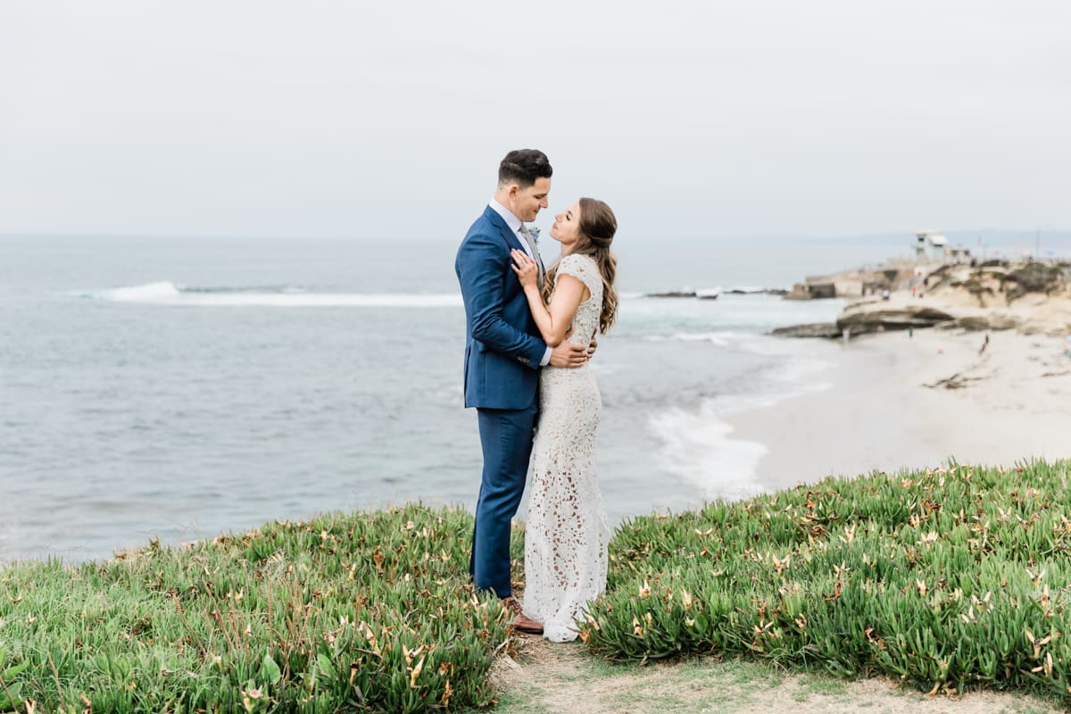 bride and groom standing on hill overlooking ocean in san diego