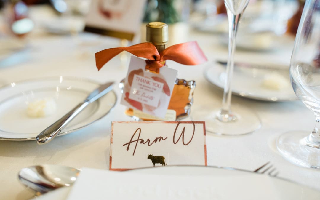 A wedding place setting with a little maple syrup bottle with a bow and a place setting card with a cow and the name Aaron W.