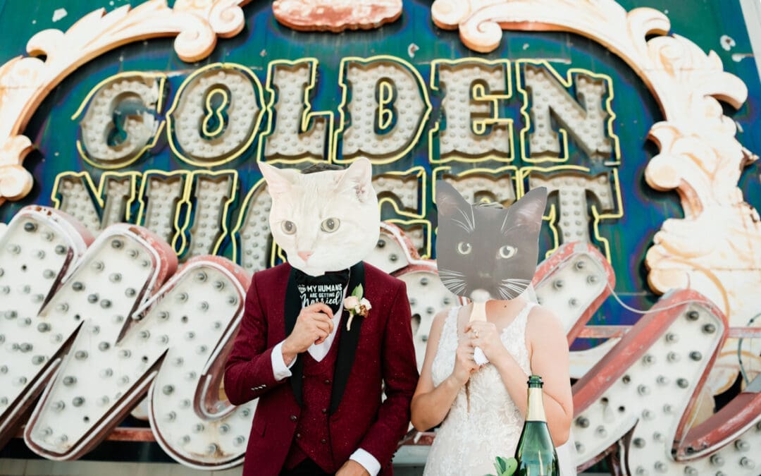 A groom and bride hold cat masks over their faces as they stand in front of defunct Vegas neon signs at the Neon Museum.